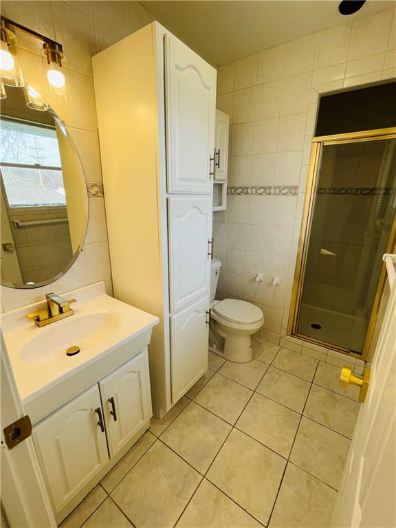 full bathroom featuring toilet, tile walls, a shower stall, tile patterned flooring, and vanity