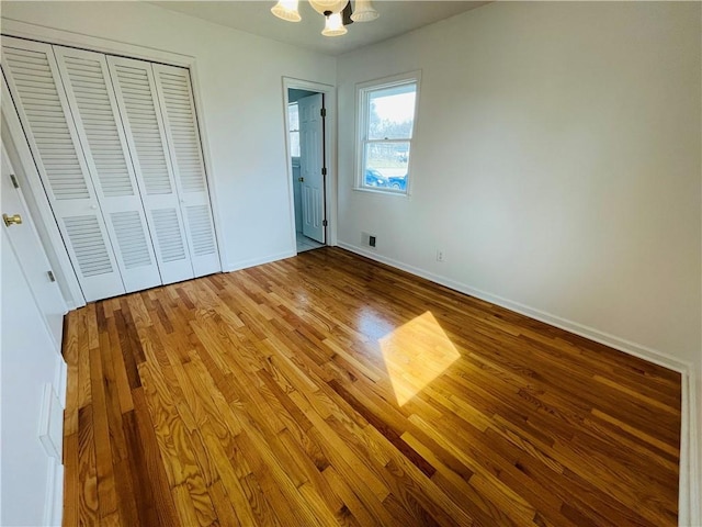 unfurnished bedroom featuring visible vents, wood finished floors, a closet, baseboards, and a chandelier