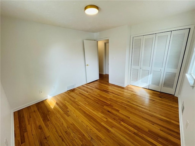 unfurnished bedroom featuring a closet, visible vents, baseboards, and wood finished floors