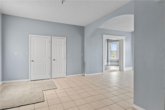 unfurnished room with light tile patterned floors, baseboards, arched walkways, and a textured ceiling