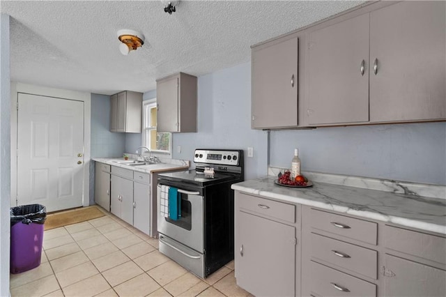 kitchen with light tile patterned floors, stainless steel electric stove, gray cabinets, light countertops, and a sink