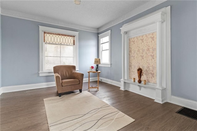 living area with a textured ceiling, visible vents, crown molding, and wood finished floors