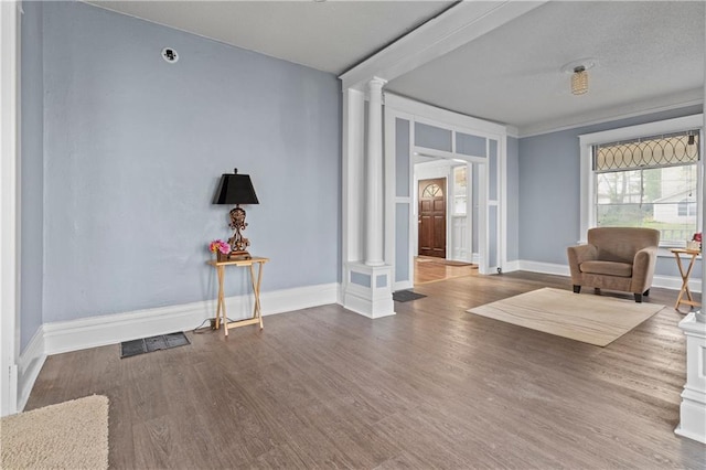 living area with ornate columns, baseboards, visible vents, and wood finished floors