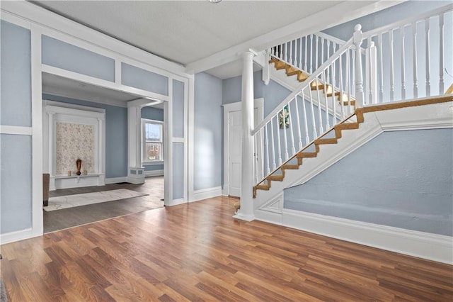 entrance foyer with decorative columns, stairway, baseboards, and wood finished floors