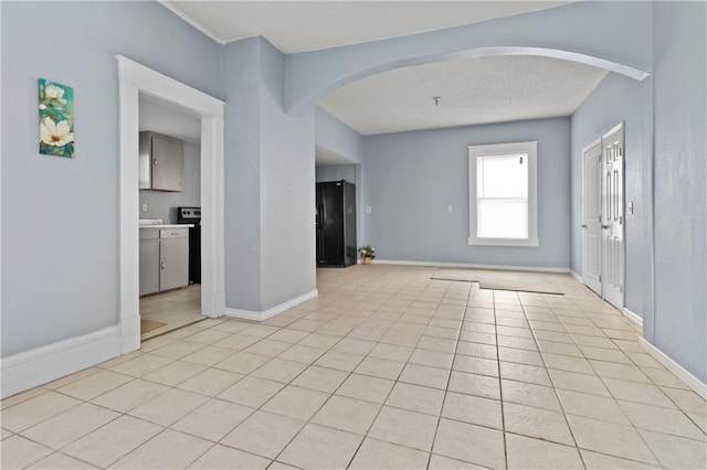 empty room featuring arched walkways, light tile patterned flooring, and baseboards