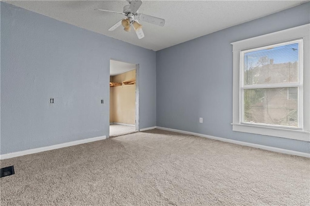 empty room featuring a textured ceiling, a ceiling fan, visible vents, baseboards, and carpet