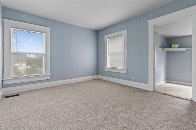 carpeted empty room featuring baseboards, visible vents, and a wealth of natural light