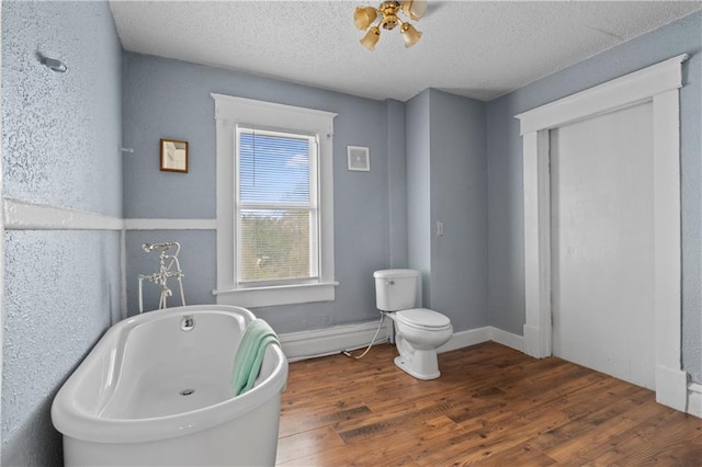 full bathroom with a soaking tub, toilet, a textured ceiling, wood finished floors, and baseboards