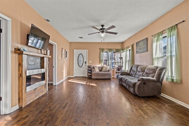 living room with a textured ceiling, baseboards, dark wood-type flooring, and a ceiling fan