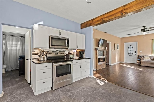 kitchen with dark countertops, open floor plan, white cabinetry, appliances with stainless steel finishes, and ceiling fan