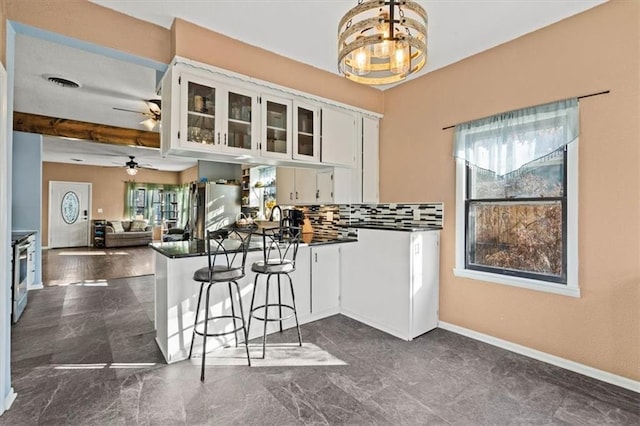 kitchen featuring a peninsula, stainless steel electric range, white cabinetry, dark countertops, and ceiling fan with notable chandelier