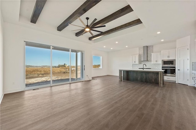 unfurnished living room with dark wood-style flooring, a sink, a ceiling fan, baseboards, and beam ceiling