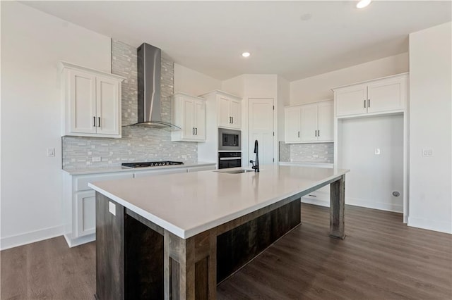 kitchen featuring wall chimney range hood, dark wood-type flooring, a large island with sink, black appliances, and white cabinetry