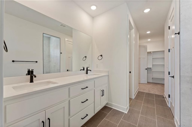 bathroom with double vanity, a walk in closet, a sink, and recessed lighting