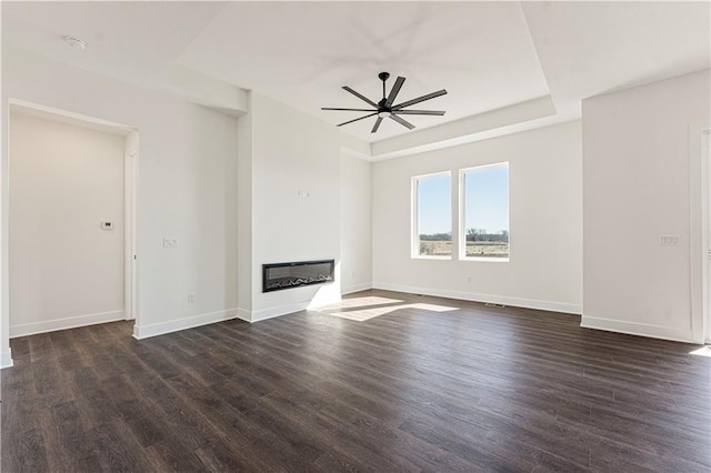 unfurnished living room featuring dark wood-style floors, ceiling fan, a raised ceiling, and a glass covered fireplace