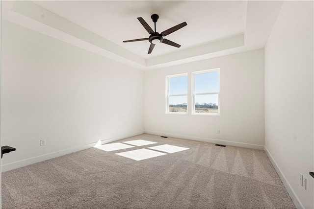 carpeted empty room with a tray ceiling, visible vents, ceiling fan, and baseboards