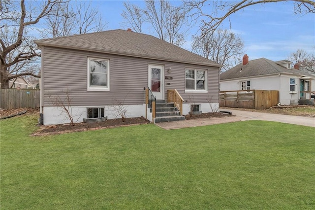 rear view of property with entry steps, fence, a lawn, and roof with shingles