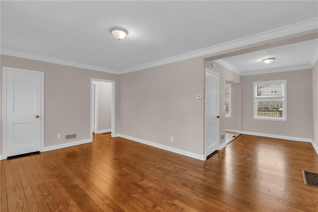 empty room with crown molding, wood-type flooring, visible vents, and baseboards