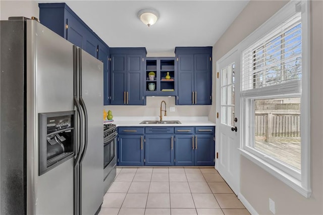 kitchen featuring light tile patterned floors, gas range oven, blue cabinetry, stainless steel refrigerator with ice dispenser, and a sink