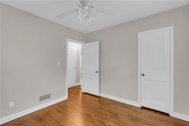 unfurnished bedroom featuring a ceiling fan, visible vents, baseboards, and wood finished floors