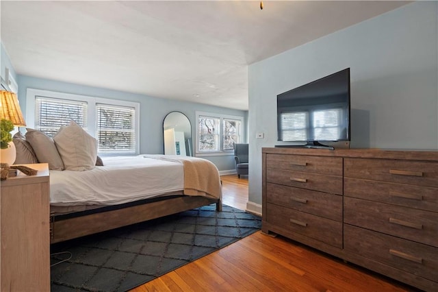 bedroom with multiple windows, baseboards, and wood finished floors