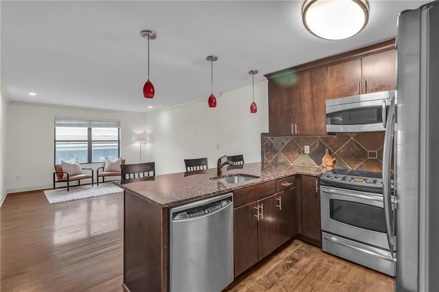 kitchen with a peninsula, a sink, appliances with stainless steel finishes, dark wood-style floors, and tasteful backsplash