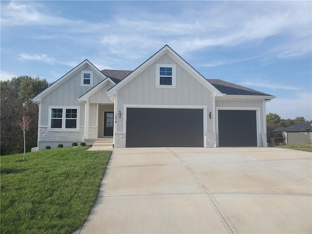 view of front of house with driveway, stone siding, roof with shingles, a front lawn, and board and batten siding