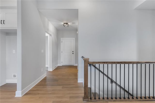 corridor featuring light wood-type flooring, baseboards, and an upstairs landing