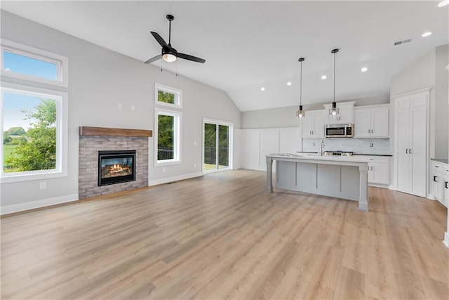 kitchen with light wood finished floors, white cabinets, decorative backsplash, stainless steel microwave, and hanging light fixtures