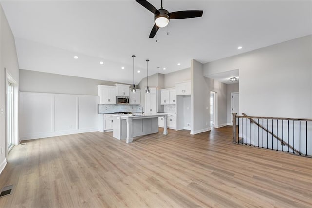 kitchen with stainless steel microwave, decorative backsplash, light wood-style floors, open floor plan, and white cabinetry