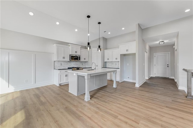 kitchen featuring white cabinets, stainless steel microwave, backsplash, and an island with sink