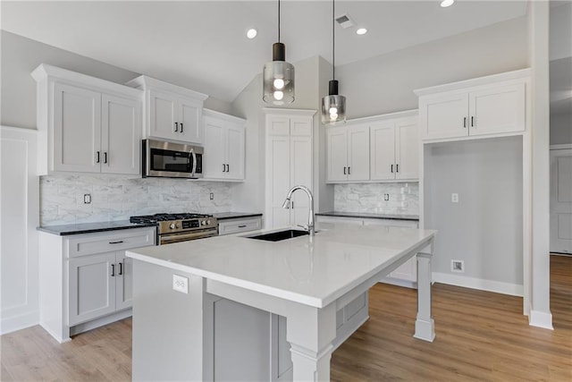 kitchen with light wood finished floors, appliances with stainless steel finishes, white cabinets, and a sink