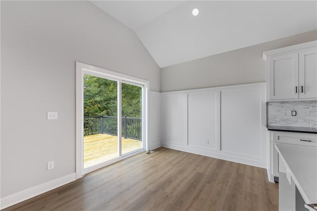 interior space featuring vaulted ceiling, a decorative wall, wood finished floors, and baseboards