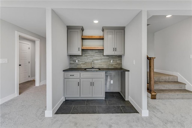 kitchen featuring tasteful backsplash, dark colored carpet, gray cabinetry, open shelves, and a sink