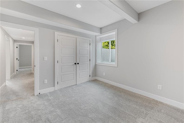 unfurnished bedroom with a closet, carpet flooring, beam ceiling, and baseboards