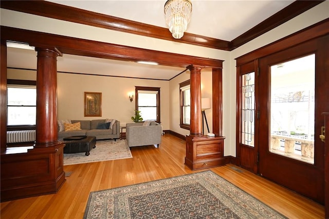 entrance foyer featuring wood finished floors, radiator, crown molding, decorative columns, and baseboards