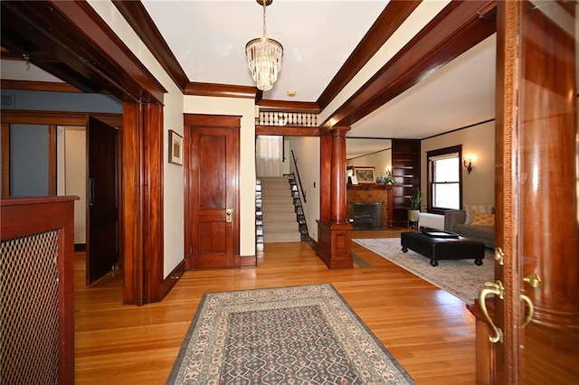 entrance foyer featuring light wood finished floors, ornate columns, an inviting chandelier, a fireplace, and crown molding