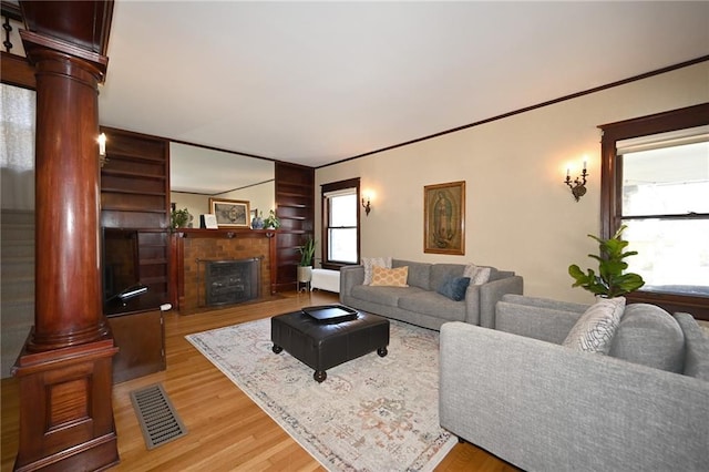 living room featuring light wood-style floors, decorative columns, a fireplace, and visible vents