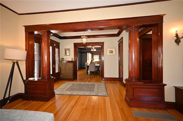 entryway featuring baseboards, wood finished floors, crown molding, and ornate columns