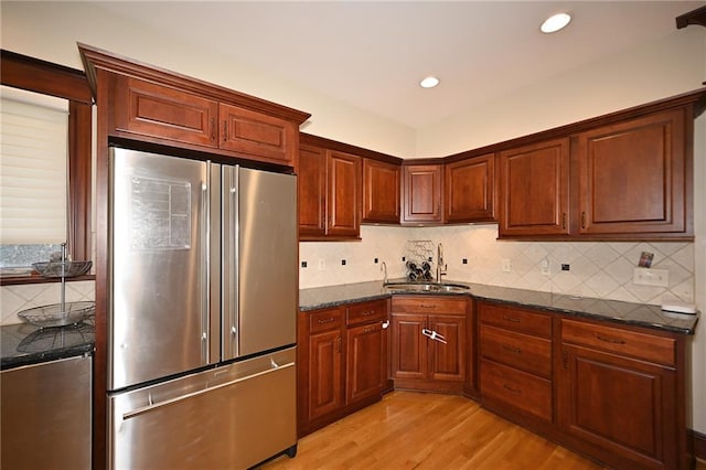 kitchen featuring light wood finished floors, dark stone counters, decorative backsplash, high end fridge, and a sink