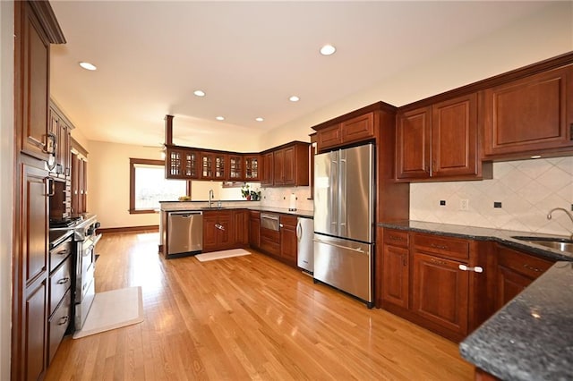 kitchen featuring glass insert cabinets, light wood-type flooring, decorative backsplash, stainless steel appliances, and a sink