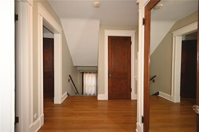 hall featuring wood finished floors, an upstairs landing, baseboards, and vaulted ceiling