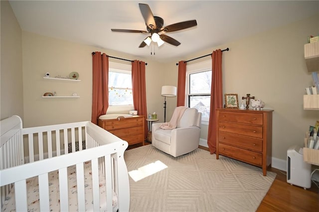 bedroom featuring multiple windows, a crib, baseboards, and ceiling fan