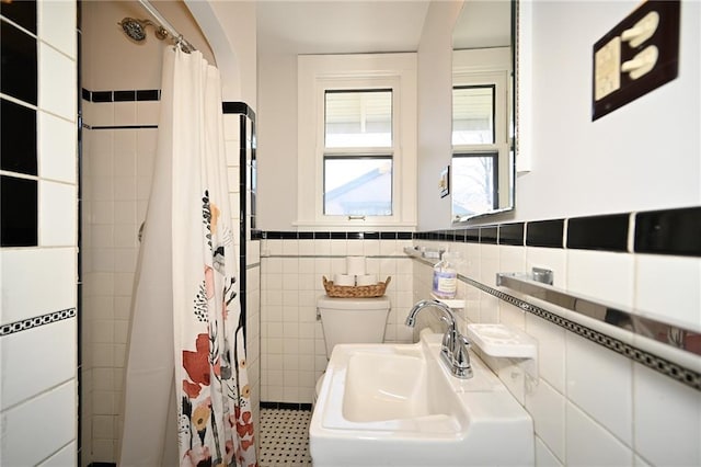 bathroom featuring a wainscoted wall, toilet, a sink, a shower with shower curtain, and tile walls