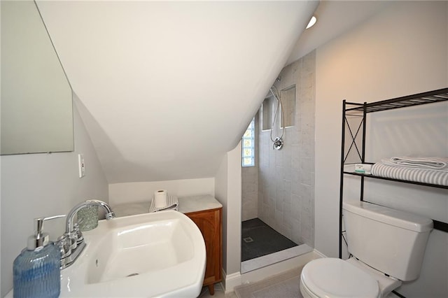 bathroom featuring vaulted ceiling, toilet, tiled shower, and a sink