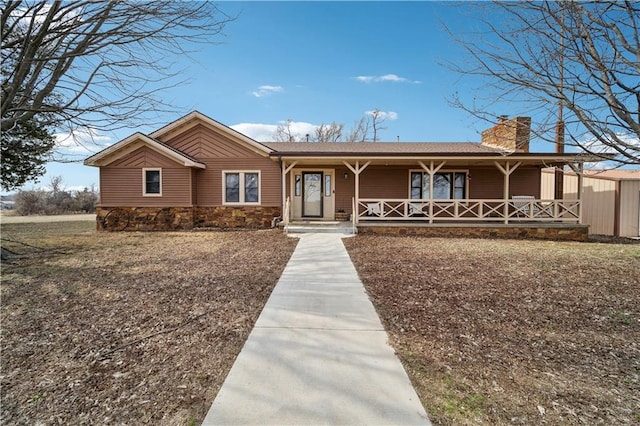 single story home featuring covered porch, stone siding, and a chimney