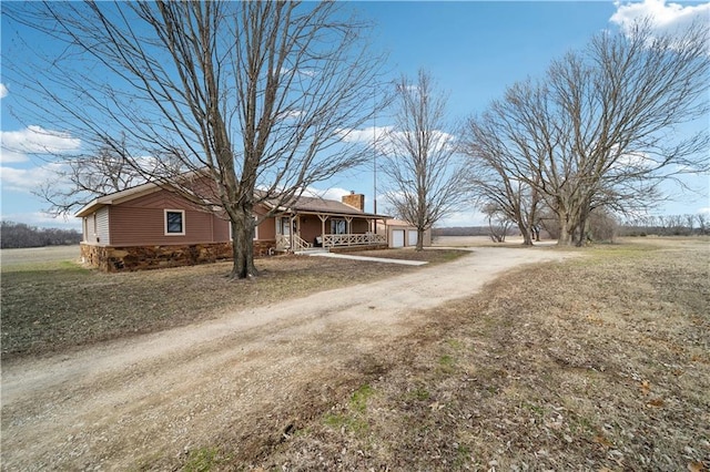 view of front of home with dirt driveway, a chimney, covered porch, and a garage