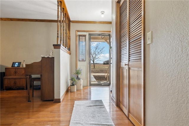 doorway to outside with a textured wall, baseboards, crown molding, and light wood finished floors