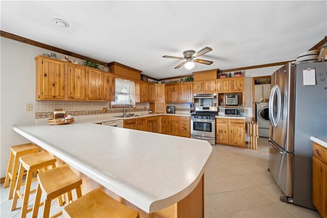 kitchen featuring light countertops, appliances with stainless steel finishes, a sink, washer / dryer, and a peninsula