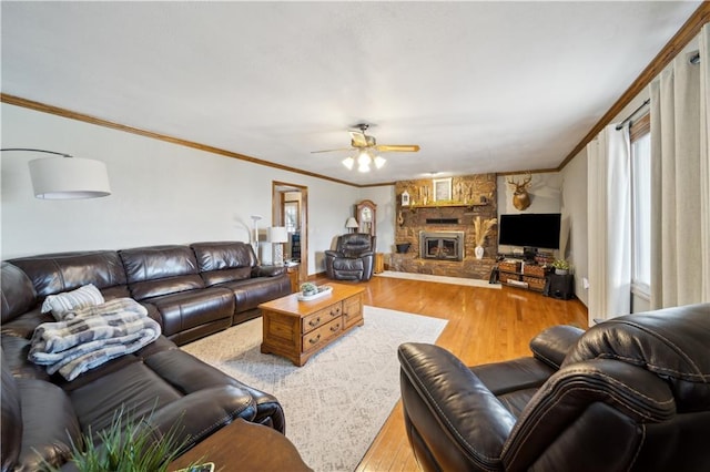 living room with crown molding, ceiling fan, wood finished floors, and a stone fireplace